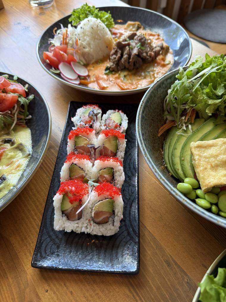 Sushi-Rollen auf einer Schieferplatte, daneben eine Bowl mit Avocado und Edamame